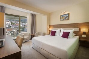 Ein Hotelzimmer mit einem großen Bett, zwei Nachttischen, einem Schreibtisch und einem Stuhl. Ein Fenster bietet Blick auf Gebäude, und an der Wand hängt ein Bild.