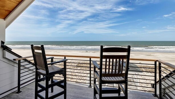 Ein Balkon mit zwei Holzstühlen mit Blick auf einen Strand.
