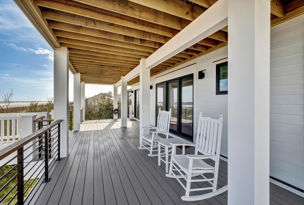 A covered deck with white rocking chairs and a wooden ceiling.