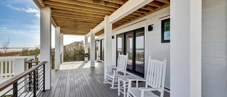 A covered deck with white rocking chairs and a wooden ceiling.