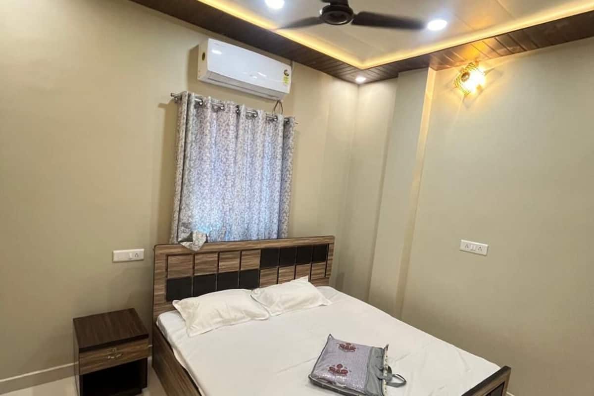A bedroom with a bed, nightstand, ceiling fan, air conditioning unit, and a window with curtains.