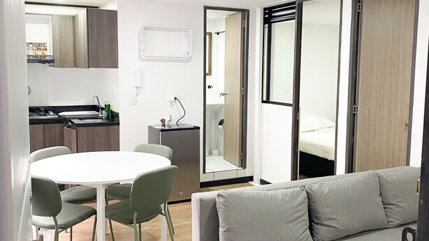A modern living space with a grey sofa, a round dining table with chairs, a kitchen area, and a large mirror. - Centrally located apartment near airport, terminal, US Embassy (Bogotá)