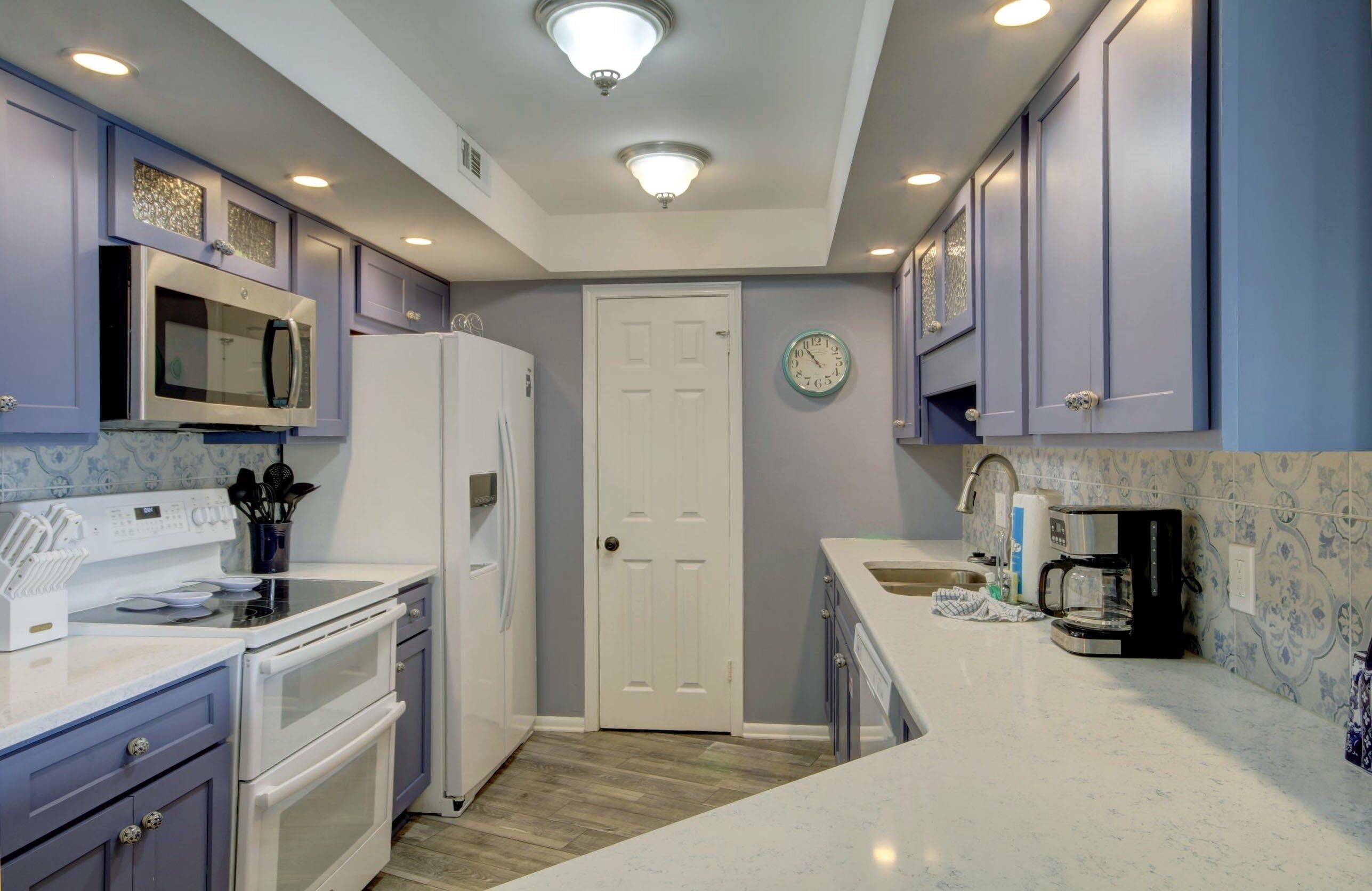 A kitchen with white appliances, blue cabinets, and a clock on the wall.
