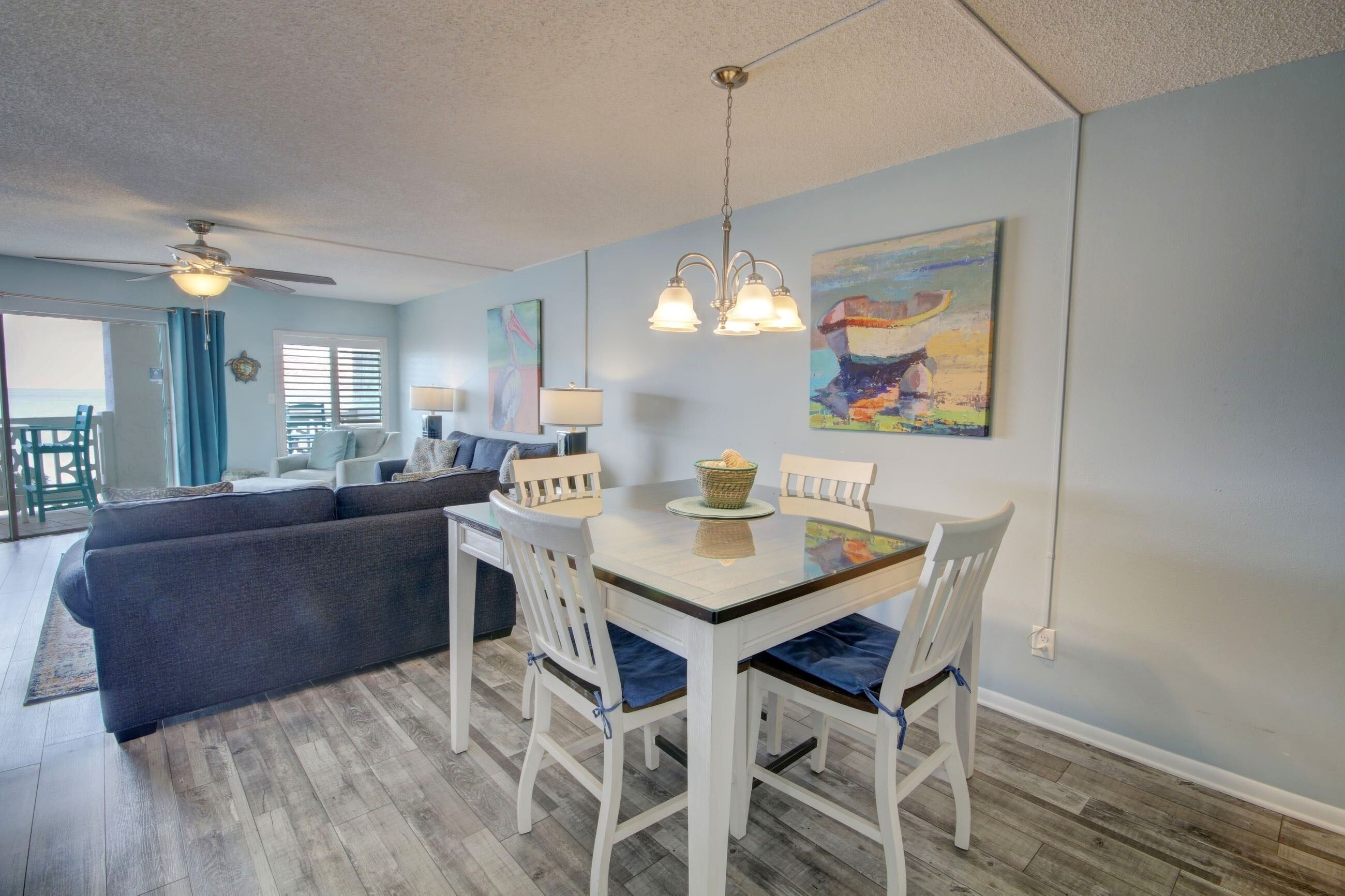A dining area with a white table and chairs, a ceiling fan, and a painting on the wall.