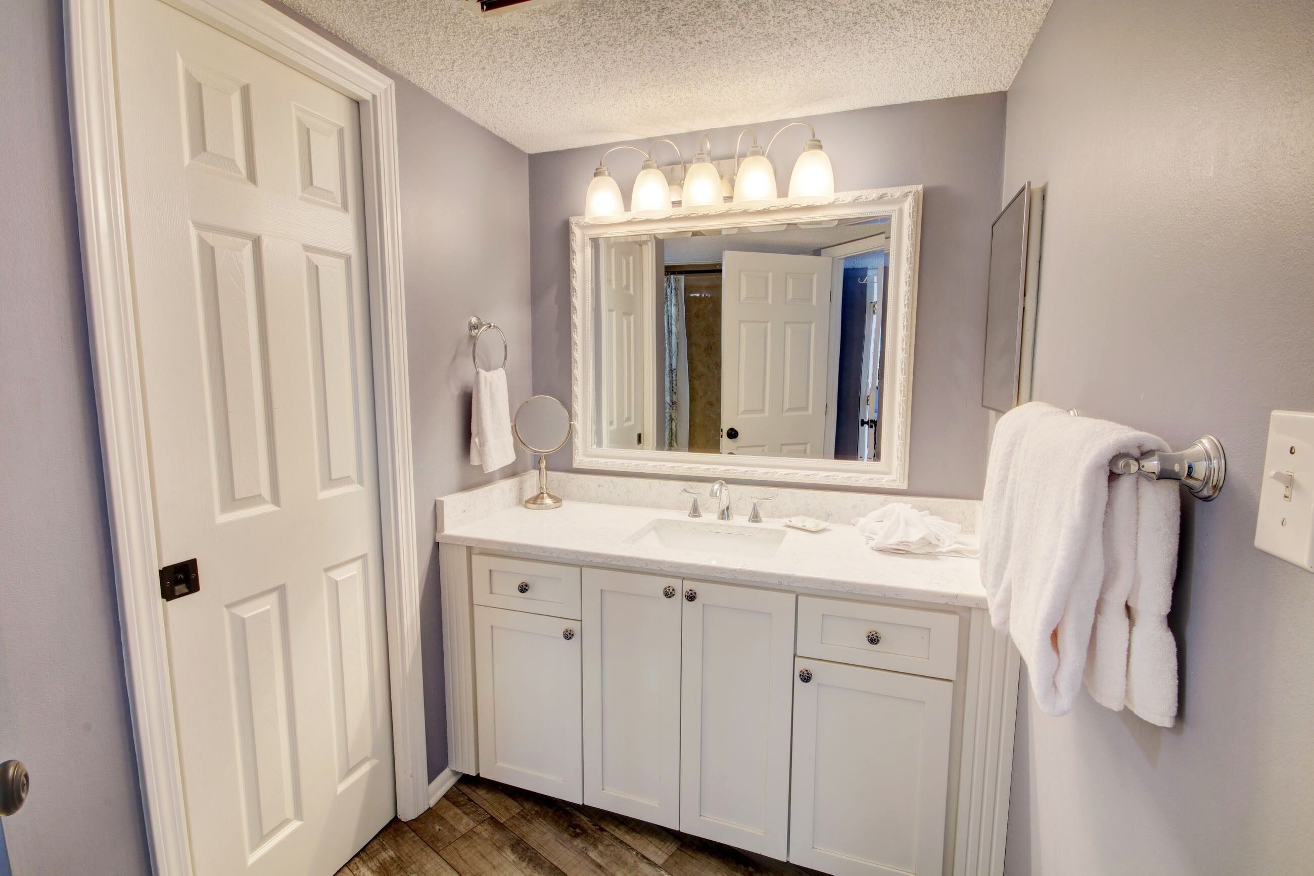 A bathroom with white cabinets, a sink, a mirror with lights, and a towel rack.
