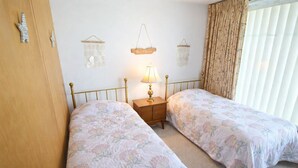 A bedroom with two single beds, a bedside table with a lamp, and a wall-mounted shelf with decorative items. - Spectacular Ocean Front Condo Downtown Rehoboth Beach, Delaware! (Rehoboth Beach)