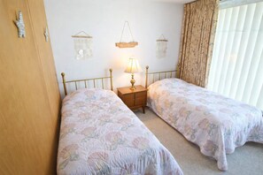 Ein Schlafzimmer mit zwei Einzelbetten, einem Nachttisch mit Lampe und einem an der Wand befestigten Regal mit Dekoration.