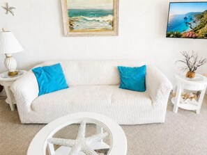 A white sofa with blue cushions, a starfish decoration, and a framed painting of a coastal scene. - Spectacular Ocean Front Condo Downtown Rehoboth Beach, Delaware! (Rehoboth Beach)