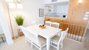 A white dining table with four chairs, a fruit bowl, a potted plant, and a modern kitchen in the background. - Spectacular Ocean Front Condo Downtown Rehoboth Beach, Delaware! (Rehoboth Beach)