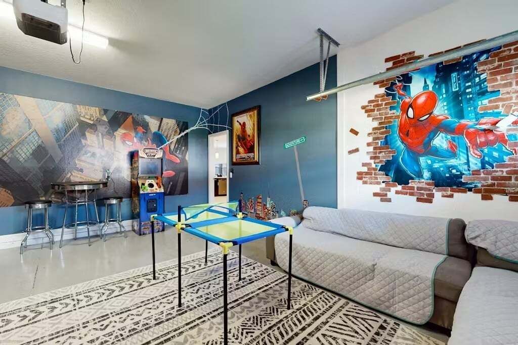 A room with a blue wall, a Spiderman mural, a sofa, a small table, and a patterned rug.