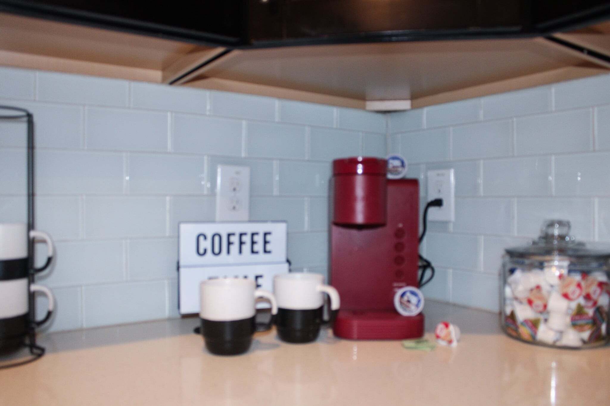 A kitchen with a coffee maker, a sign that says 'COFFEE,' and a jar of candies.