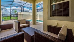 Un espace extérieur aménagé, abrité et doté de mobilier en osier, d’une structure en verre et offrant une vue sur une piscine.