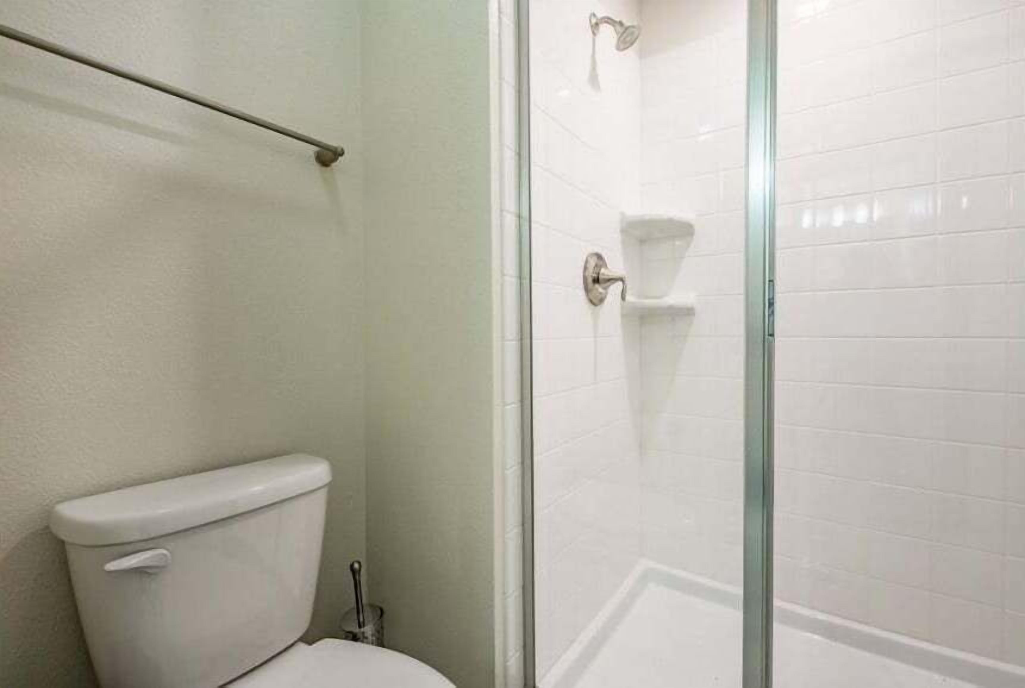 A bathroom with a toilet, a glass shower enclosure, and a white tiled wall.