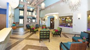 Un hall d’entrée spacieux avec un plafond haut, des poutres en bois et un espace de détente central agrémenté de chaises et d’une table.