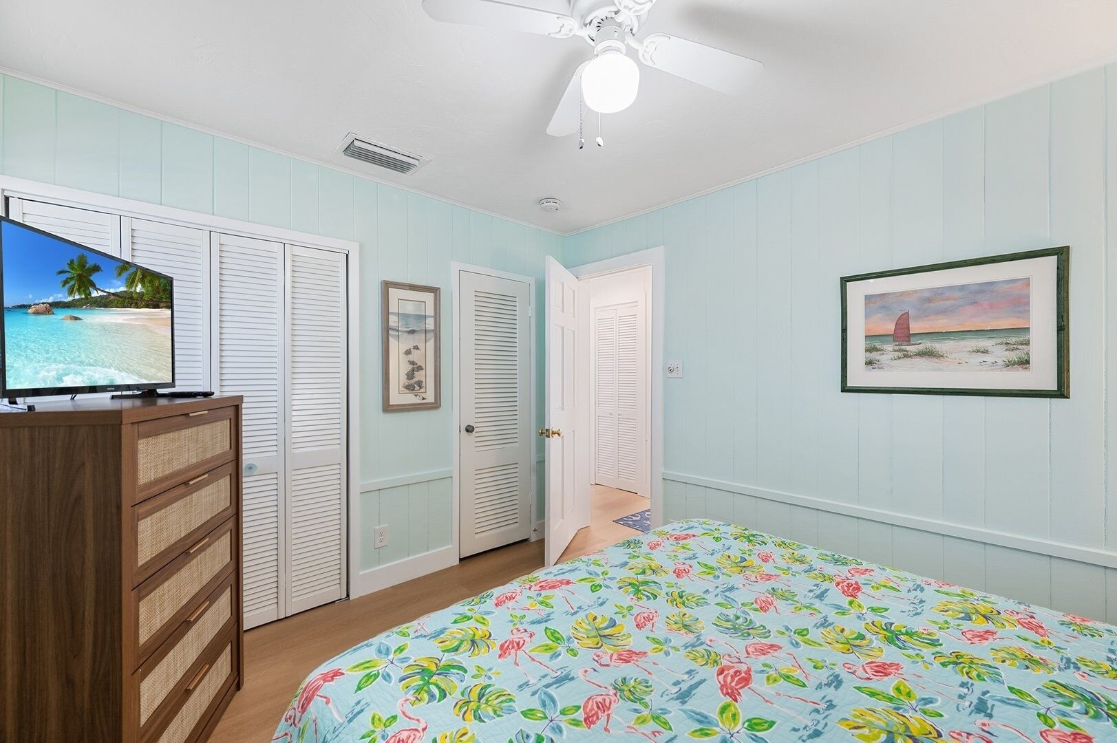 Une chambre à coucher comprenant un lit, une commode, un ventilateur de plafond et un téléviseur.