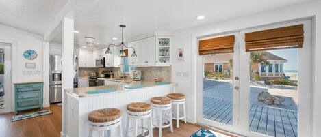 A kitchen with a central island, white cabinets, and a view of the beach through a sliding door.