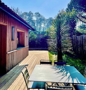 Una terraza de madera con una mesa y sillas, rodeada por una valla de madera y varios árboles.
