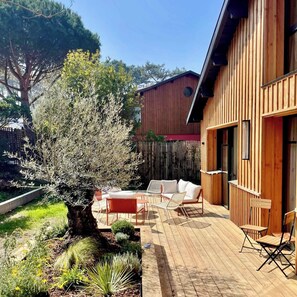 Eine Holzterrasse mit Gartenmöbeln, einem Baum und einem Gebäude mit senkrechter Holzverkleidung.