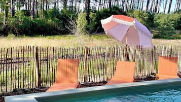 Una piscina con cubierta de madera, rodeada por una cerca de bambú y una sombrilla de playa.