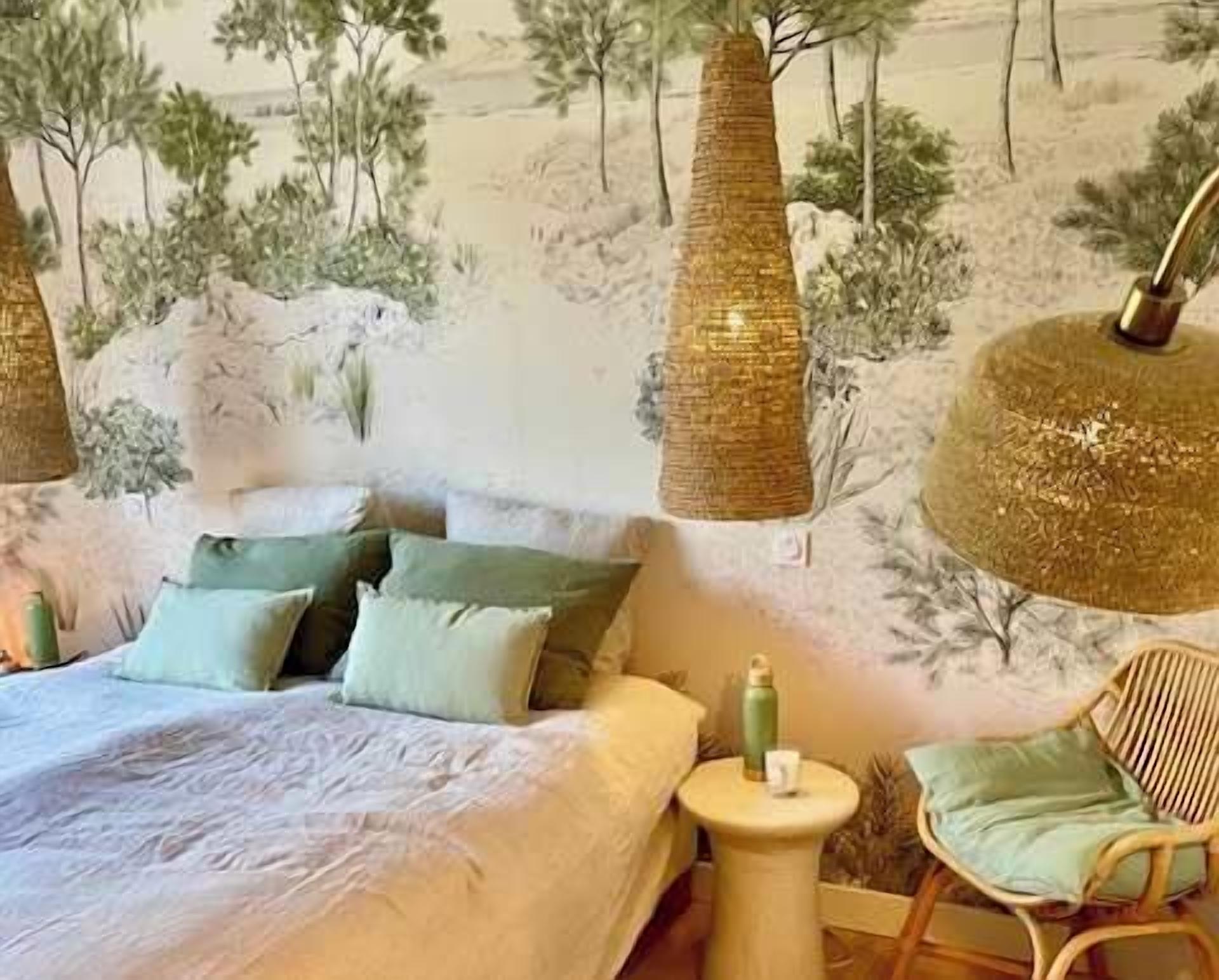 A bedroom with a bed, pillows, a side table, a chair, and a wall mural.