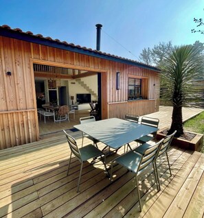 Una casa de madera con una terraza, una mesa de comedor y sillas.