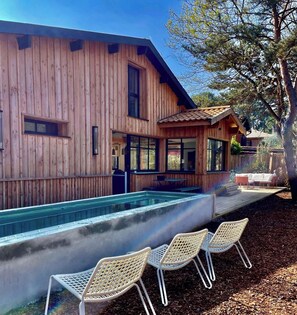 En træbygning med swimmingpool og udendørs siddepladser.