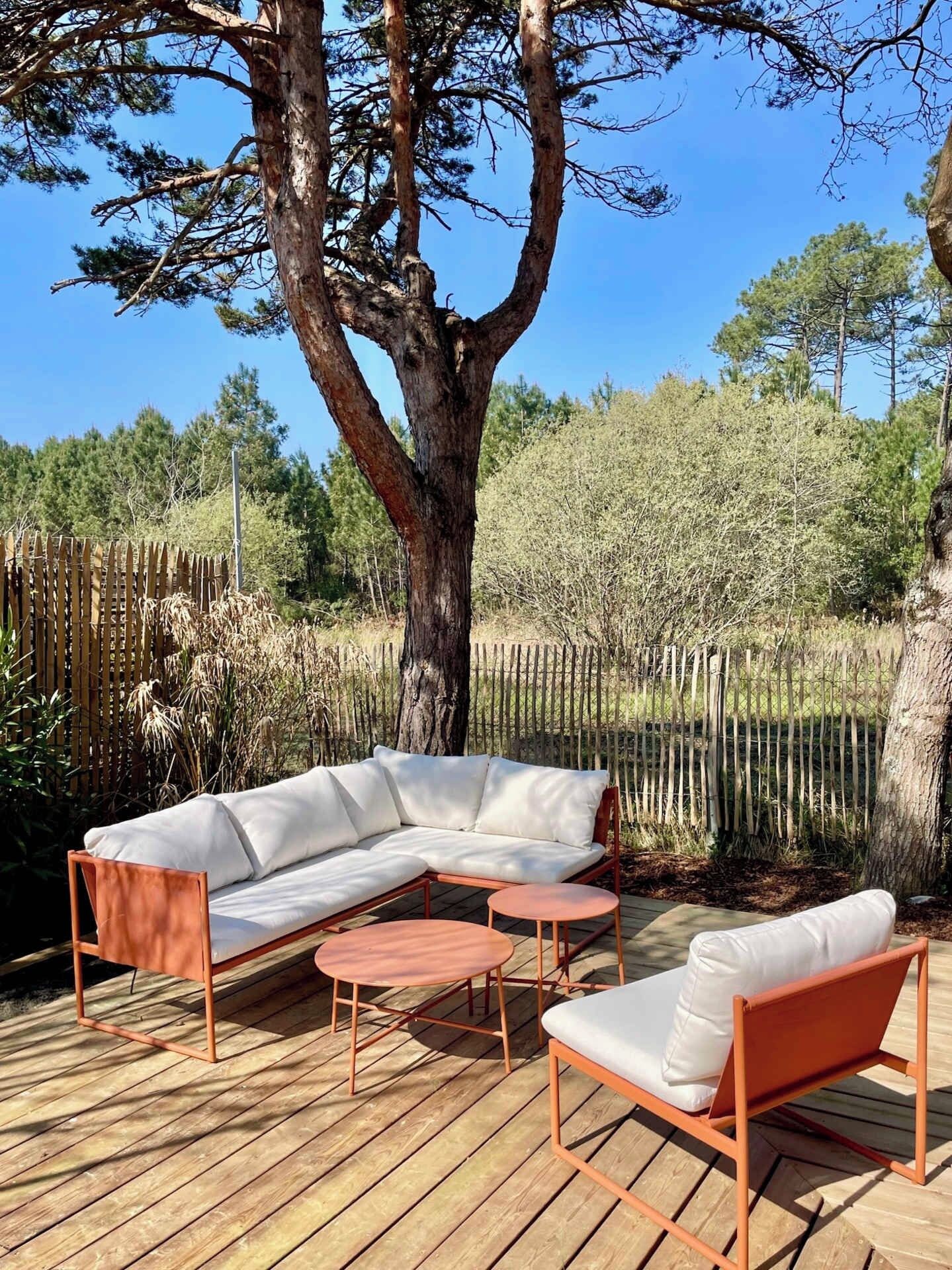 Una terraza de madera con un sofá modular y dos mesas redondas.