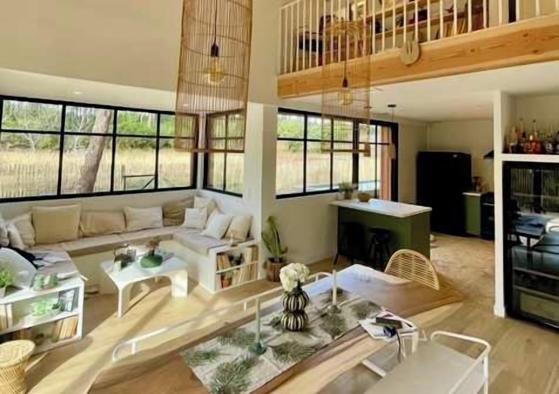 Un espacio habitable amplio con techos altos, ventanas grandes, una mesa de comedor y un conjunto de asientos.