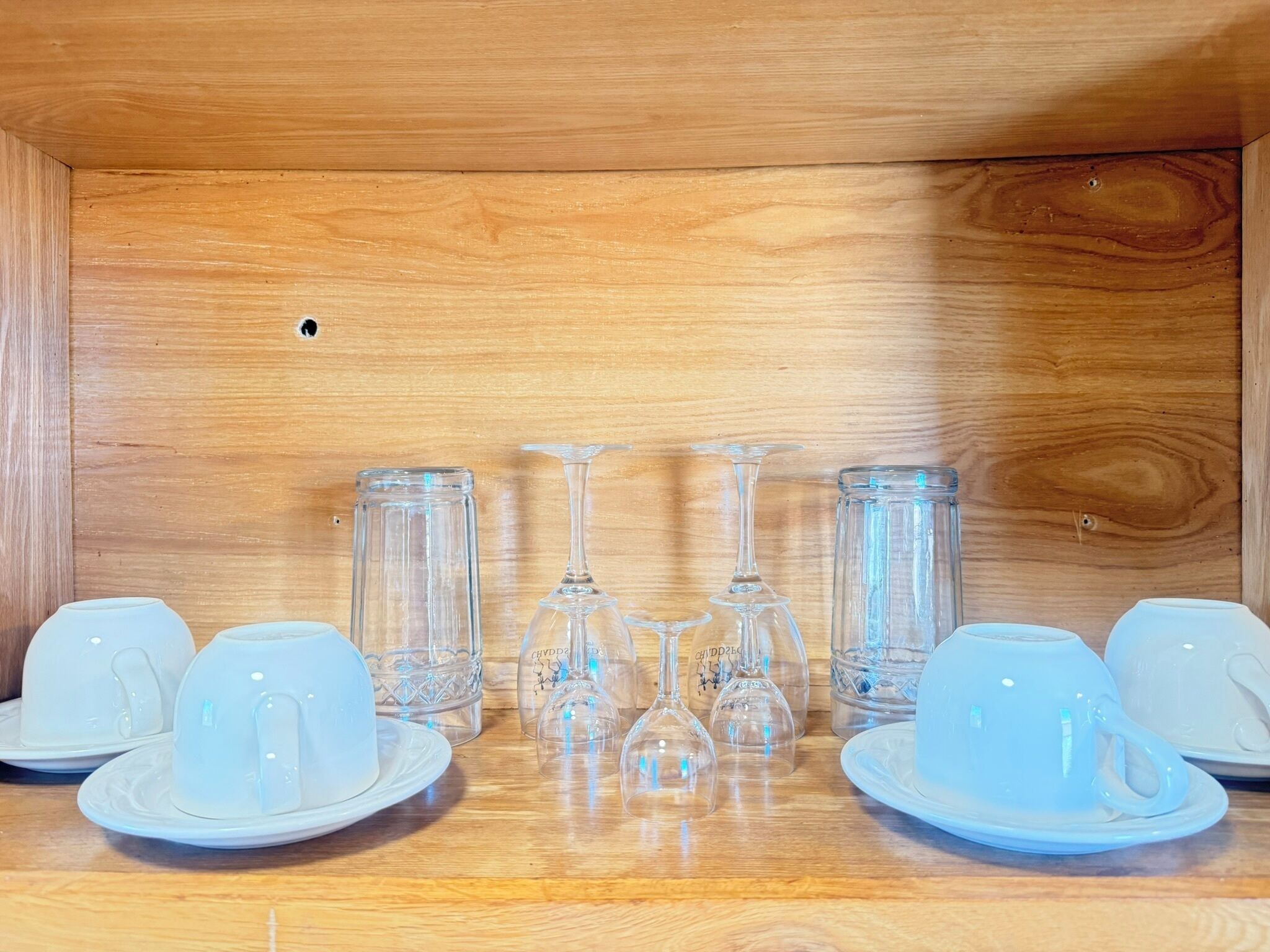 A wooden cabinet with a mirrored surface, containing a set of white cups and clear glassware.