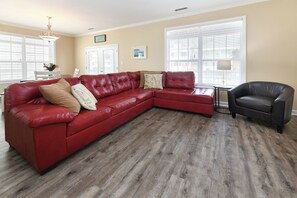 A living room with a red leather sectional sofa, a black armchair, and a wooden floor. - 5 BR,  Walk To The Beach, Private Pool - A Son Of A Sailor (Surfside Beach)