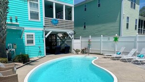 Una piscina con bordo bianco, circondata da sdraio e un'area coperta con ventilatore a soffitto.