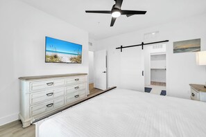 Un dormitorio con una cama, un tocador, un ventilador de techo, una puerta y un cuadro colgado en la pared.