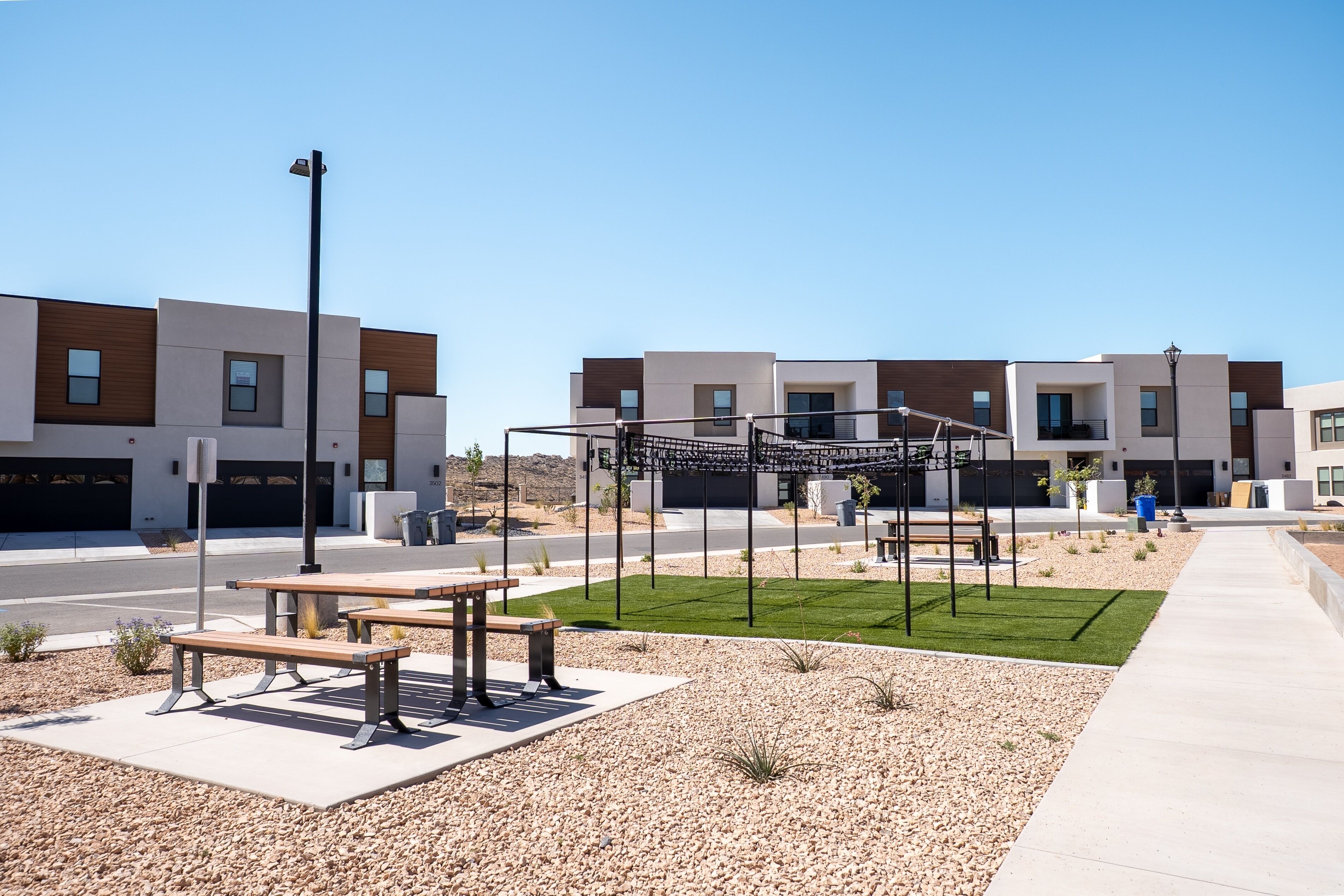 A modern residential area with a paved walkway, benches, and a playground structure.