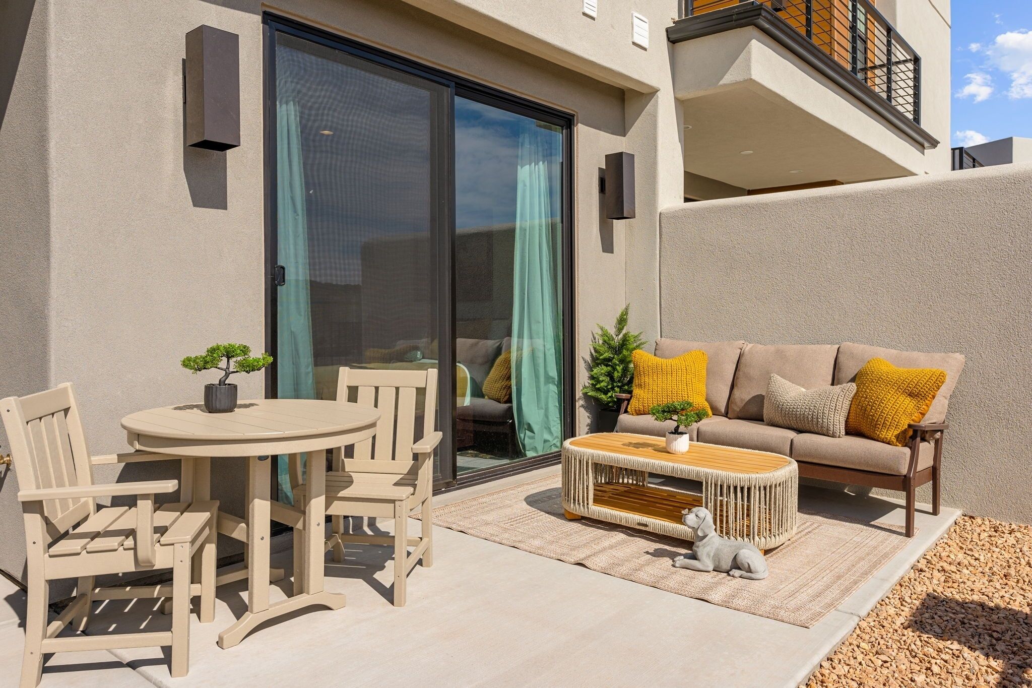 Eine Terrasse im Freien mit einem runden Tisch, zwei Stühlen, einer Couch und einem kleinen Hund.