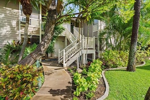 A residential building with a covered outdoor staircase, surrounded by lush greenery and a well-maintained lawn. - Grand Champions 185 2 Bedroom Condo (Kihei)