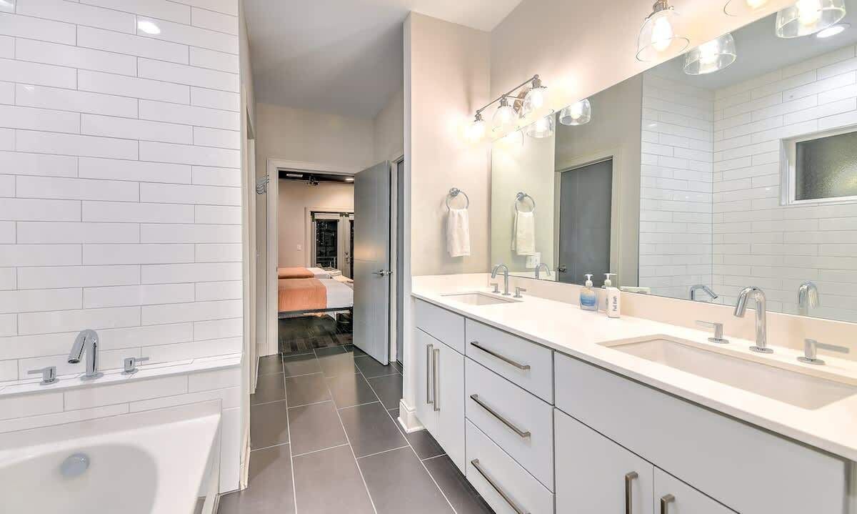 A modern bathroom with a large mirror, two sinks, and a bathtub.