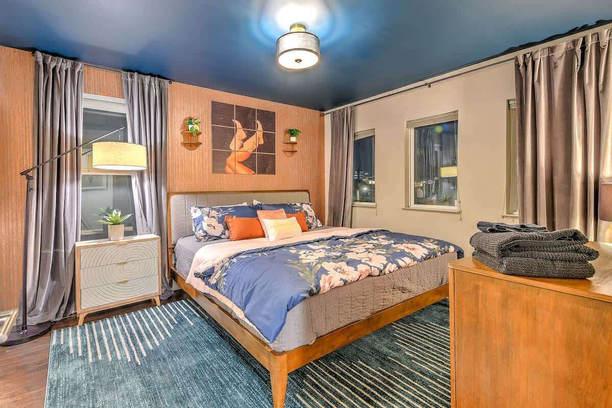 A modern bedroom with a large bed, a bedside table, a lamp, and a view of the city at night.
