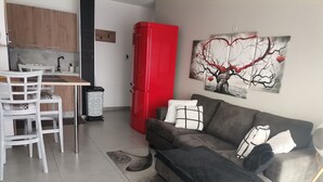 En moderne stue med en grå sofa, stole med sort og hvide mønstre, et rødt køleskab og et abstrakt billede på væggen.