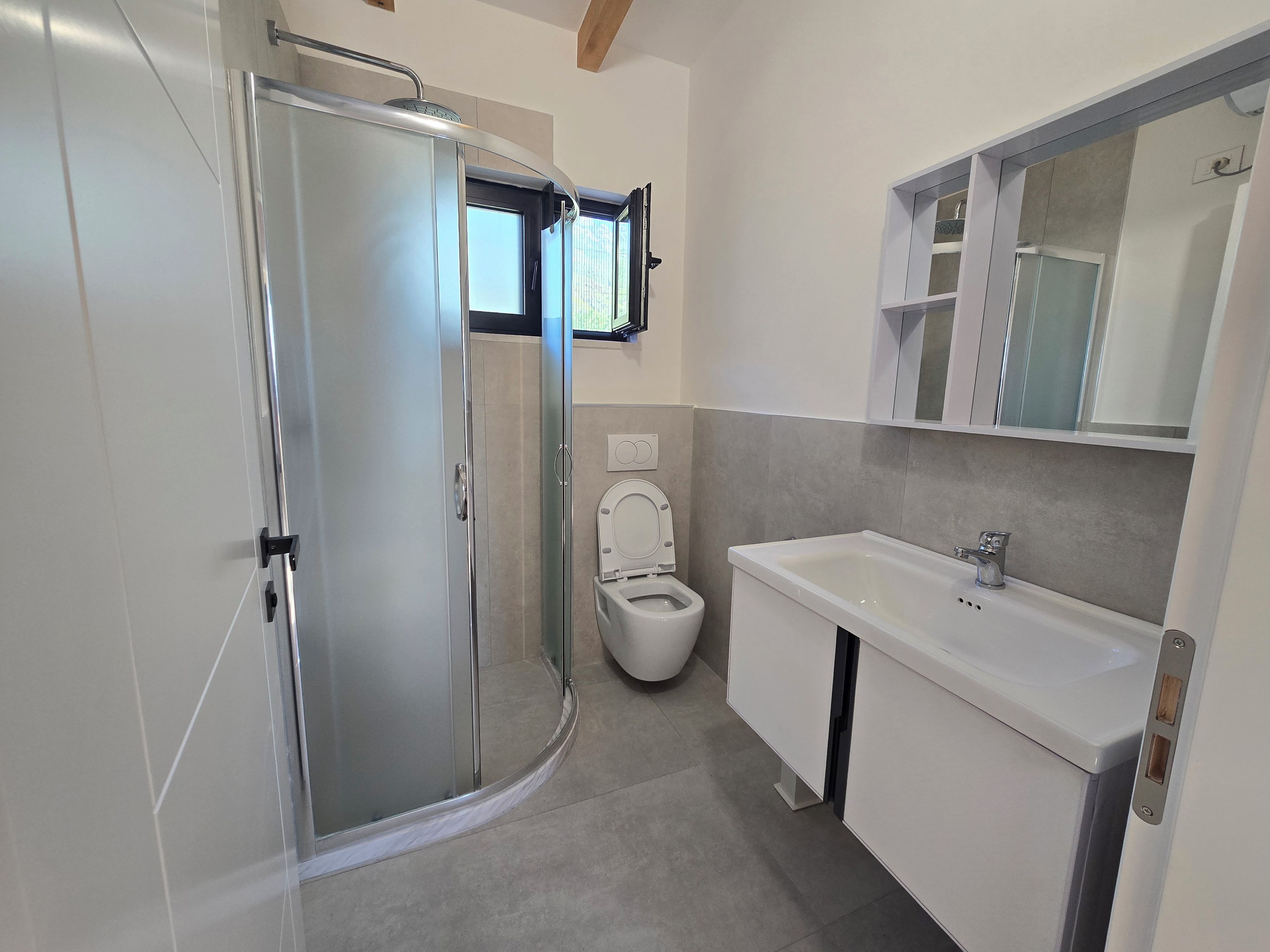 Un bagno moderno con box doccia in vetro, un water e un lavabo con pensili.