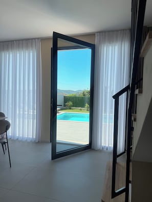 A room with a large sliding glass door leading to a pool area, a dining table, and a staircase.