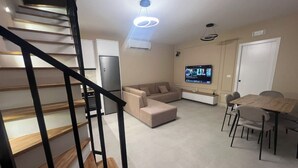 Ein modernes Wohnzimmer mit Treppe, Flachbildfernseher, Esstisch mit Stühlen und Küchenzeile.