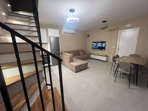 A modern living room with a staircase, a flat-screen TV, a dining table with chairs, and a kitchen area. - Poolside Bliss | Modern Villa (Kallmet i Madh)
