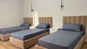 Ein Zimmer mit drei Einzelbetten, jedes mit einem hölzernen Kopfteil und einem Nachttisch.