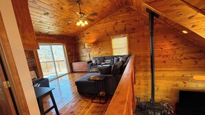 A cozy cabin interior with a wooden ceiling, a sofa set, a fireplace, and a dining table.