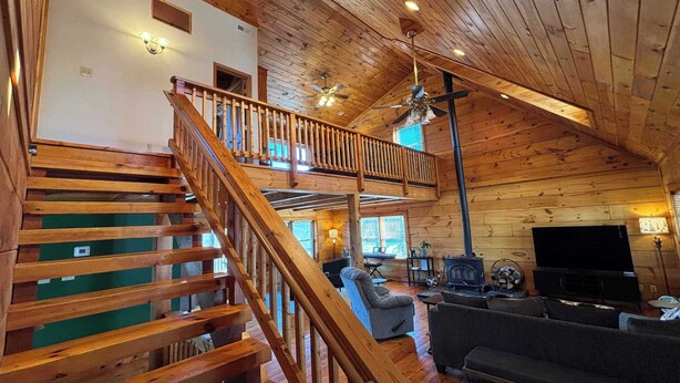 A wooden cabin interior with a wooden staircase, a living room with a sofa and a television, and a fireplace.