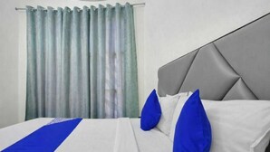 A hotel room with a bed, grey headboard, white bedding, and blue pillows. - Rathi Residency I Ambala (Ambala)