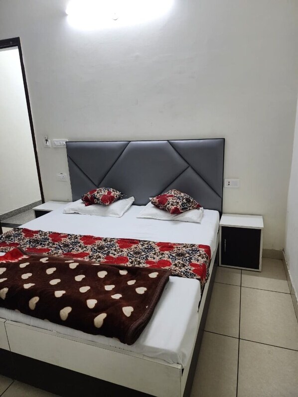 A neatly arranged bedroom with a bed, pillows, a bedside table, and a small cabinet. - Rathi Residency I Ambala (Ambala)