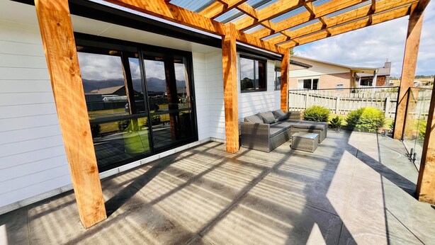A covered patio with a wooden pergola, large sliding glass doors, and a seating area with a sofa and ottoman. - Southern Peaks by Aotearoa Escapes (te anau)