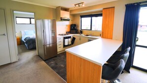 A compact kitchen with a refrigerator, stove, and sink. - Southern Peaks by Aotearoa Escapes (te anau)