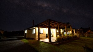 A house with a wooden structure, a porch, and a well-lit interior. - Southern Peaks by Aotearoa Escapes (te anau)